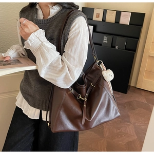 Detail view of large dark brown leather tote bag with side buckles and white bear charm