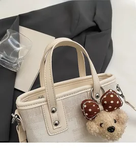 Gros plan d'un sac seau beige avec un charmant ours en peluche et des détails en métal
