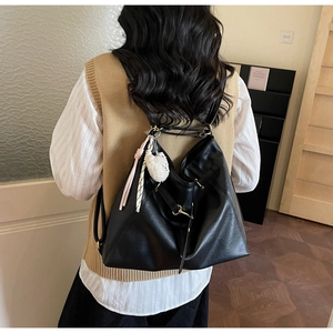 Detail view of large black leather tote backpack with white fur ball and tassel charms