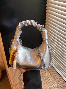 Silver metallic dumpling handbag with chain strap and bead charm on rustic wooden background