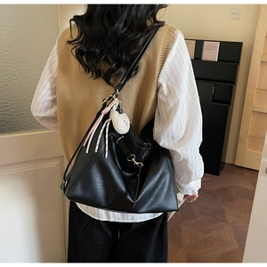 Detail of black tote bag with white plush ball and gold buckle on female model