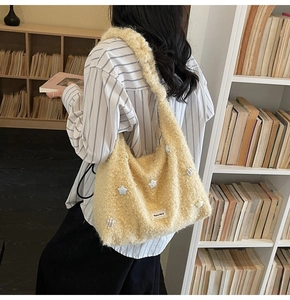 Detail of soft beige plush hobo bag with star motifs and side label shown in a cozy room