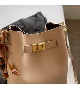 Detailed macro of beige bucket bag showing gold square lock and litchi texture leather