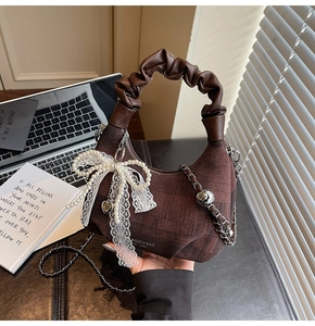 Detail view of brown dumpling bag with white lace pearl bow and metal heart charm