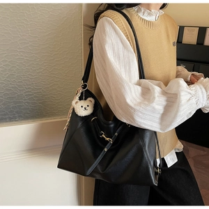 Side view of black leather tote bag with gold buckle and plush bear charm on a model