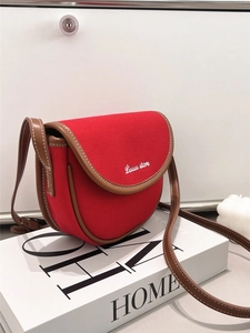 Detailed close-up of a red canvas saddle bag with brown leather trim and white embroidery