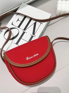 Detail of red canvas crossbody bag with brown leather trim and white embroidered text