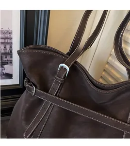 Close-up of dark brown leather tote bag with white contrast stitching and adjustable strap
