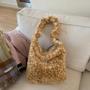Close-up detail of plush leopard print faux fur tote bag on a cozy sofa background