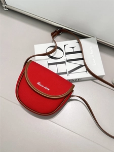 Detail of red canvas crossbody bag with brown leather trim and white stitching on cover