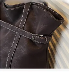 Detail of dark brown leather tote with silver buckle and white contrast stitching
