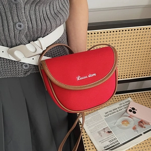 Detail of red canvas saddle bag with brown leather trim and white text logo branding