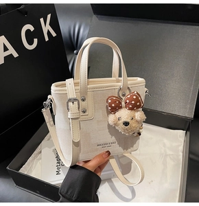 Détail d'un sac seau en toile et cuir beige avec breloque d'ours et coffret cadeau chic