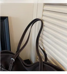 Close-up of dark brown leather tote bag with white contrast stitching and silver buckle detail