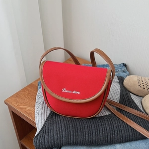 Close-up of red canvas saddle crossbody bag with brown leather trim on casual clothing