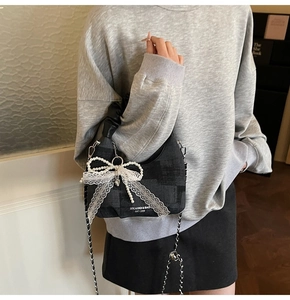 Detail of black bag with large lace pearl bow and silver heart pendant on chain