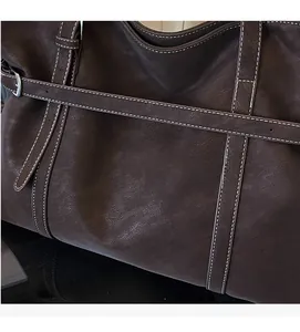 Detail of dark brown leather tote bag showing white contrast stitching and soft texture