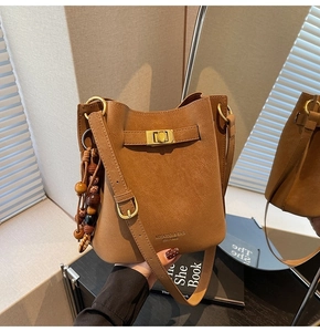 Detail of warm brown bucket bag with gold twist lock and wooden bead tassel decor