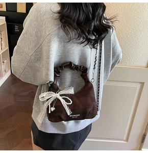 Detail view of brown dumpling bag featuring white lace bow and pearl heart charm