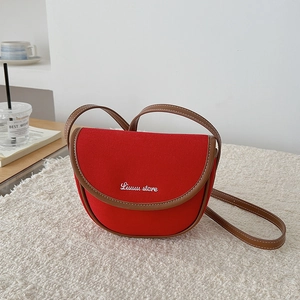 Detailed close-up of a red canvas saddle bag with brown leather trim on soft white fabric
