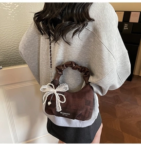 Detail view of brown dumpling bag with lace bow, pearls and heart pendant