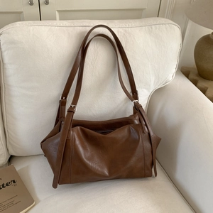Detail of vintage brown leather tote bag with double straps and metal buckles on a white sofa