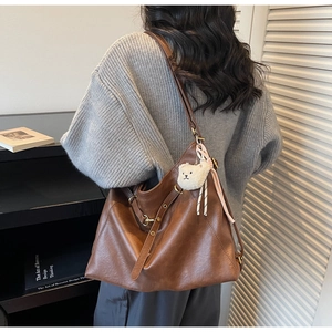 Close-up of brown faux leather tote bag featuring metal buckle and plush bear charm