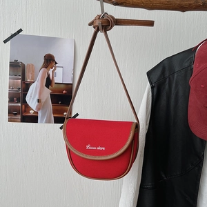 Close-up of a red canvas saddle bag with brown leather trim hanging on a wooden beam