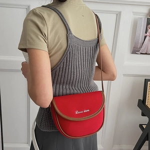Detail showing red crossbody bag with brown leather trim and silver logo lettering