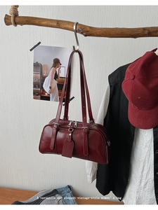 Detailed view of a dark red Boston bag with shiny leather texture hanging on a wooden branch