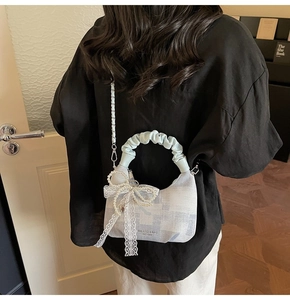Detail of light blue plaid handbag with lace bow, pearls and ruched handle on model