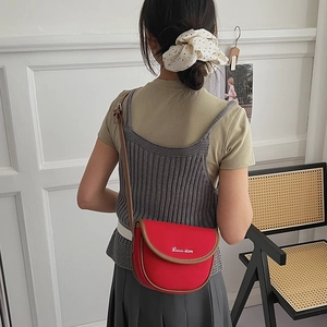 Red canvas saddle bag with brown leather trim and white branding shown on a model