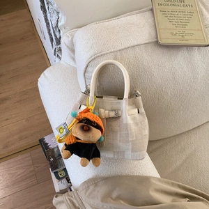 Detail der beige Eimertasche mit niedlichem Hunde-Plüsch-Anhänger auf weichem Sofa