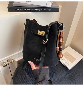Detail of black bucket bag featuring ethnic wooden bead charm and golden metal buckle