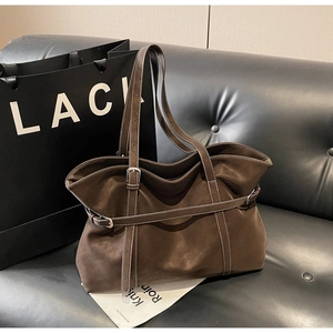 Detail of brown suede tote bag featuring contrast white stitching and metal buckles