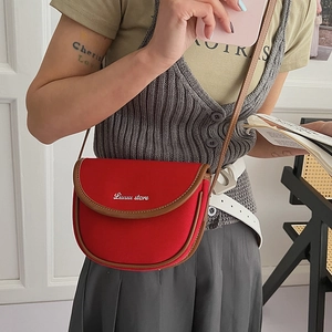 Detail of red canvas saddle bag featuring brown leather trim and white brand embroidery