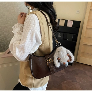 Close-up of retro brown leather crescent bag with buckle and grey bunny pendant