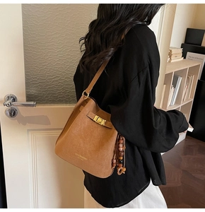 Detail of brown suede bucket bag featuring golden clasp and vintage beaded charm