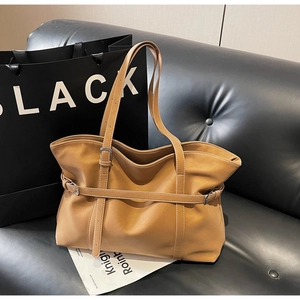 Close-up of brown vintage tote bag with adjustable straps on a black leather sofa