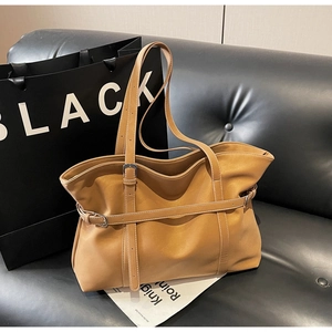 Detail of tan leather tote bag with decorative straps and buckles on a black sofa