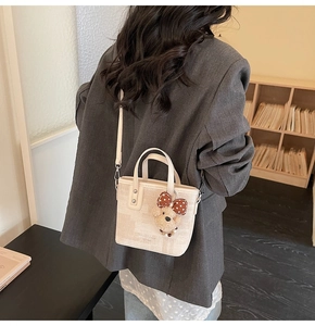 Mini sac seau tissé beige avec breloque ours porté sur un blazer anthracite