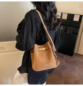 Detail of brown suede bucket bag featuring a turn-lock closure and decorative wooden beads