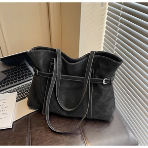 Macro view of large black leather tote bag with white stitching and metal adjustment buckle