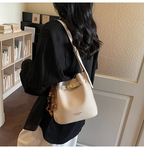 Detail of light beige bucket bag showing gold twist lock and wooden beaded tassel charm