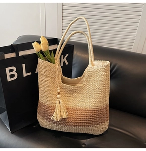 Detailed view of woven straw tote bag with wood bead tassel charm on a black leather sofa