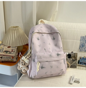 Detail view of purple nylon backpack featuring grey butterfly prints and a cute bear charm