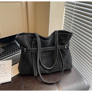 Detail of black tote bag featuring white contrast stitching and decorative silver buckle straps