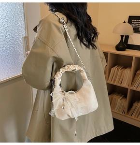 Detail of cream pleated dumpling bag featuring lace pearl bow and gold chain strap