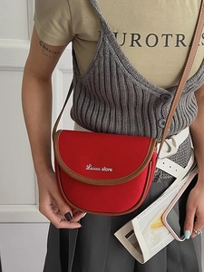 Red canvas saddle bag with brown leather trim and embroidery worn by an Asian model