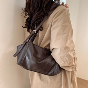Detail of dark brown vintage crescent saddle bag in soft faux leather worn with trench coat